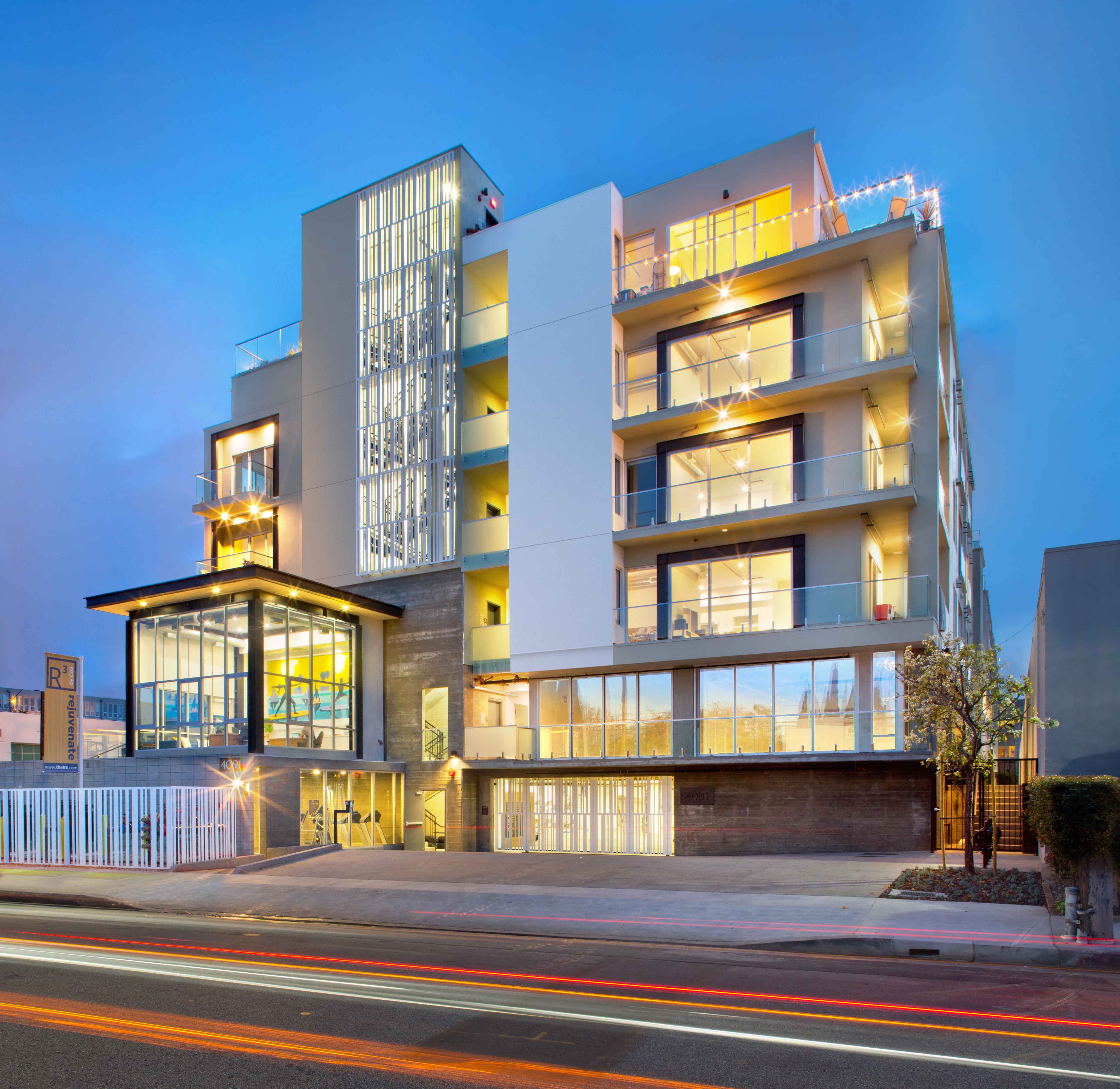 A modern building with a glass facade and a lit up balcony.